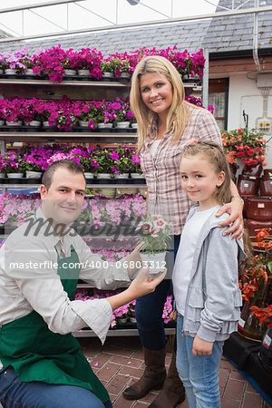 Employee giving flower pot to little girl with mother in garden center