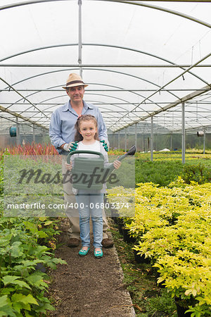 Gardener and granddaughter holding a watering can in greenhouse