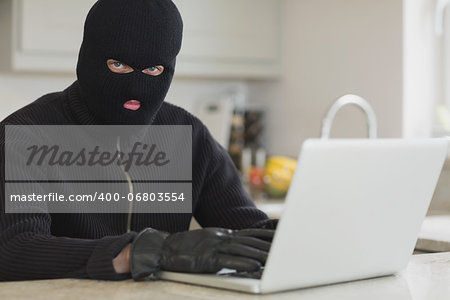 Burglar using laptop sitting in kitchen
