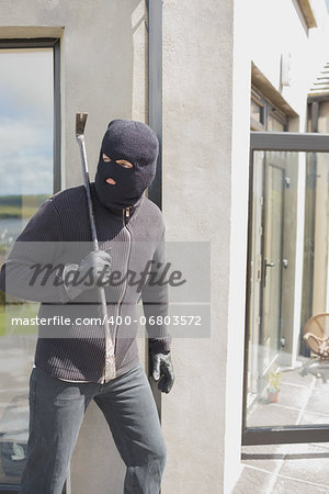 Burglar hiding behind wall with crow bar in back garden