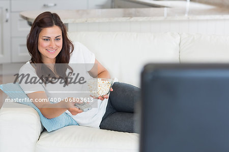 Brunette changing channel on tv on sofa with popcorn