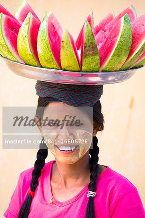 Local woman with Thanakha traditional face painting, carrying a tray of sliced watermelon on her head, Shwezigon Paya, Nyaung U, Myanmar (Burma), Asia