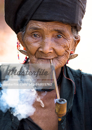 Woman of the Ann tribe in traditional black dress smoking a pipe outside a hill village near Kengtung (Kyaingtong), Shan State, Myanmar (Burma), Asia