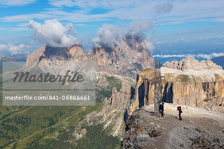 Tourists near cross on Sass Pordoi mountain in the Dolomites near Canazei, with Sassolungo mountains in the distance, Italy, Europe