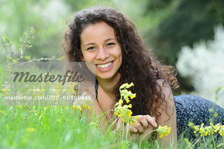 Young woman lying on a meadow beside cowslips in spring, Germany
