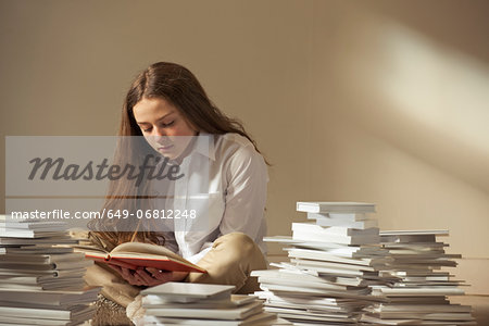 Girl sitting on floor reading surrounded by piles of books