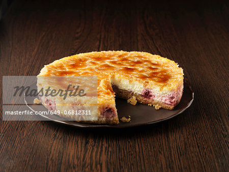 Lemon and raspberry brulee cheesecake on dark brown plate and surface