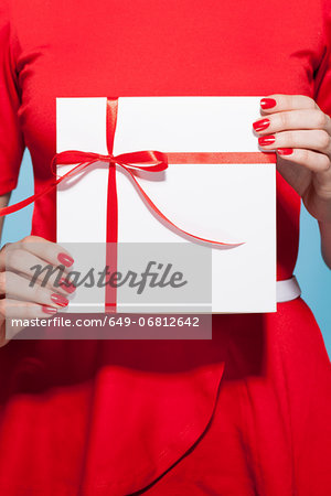 Woman holding white gift box with red bow, mid section