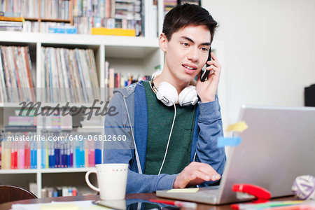 Male student on cell phone using laptop