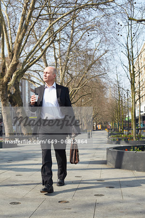 Mature businessman walking on sidewalk with coffee