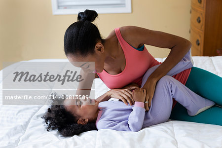 Mother tickling daughter on bed