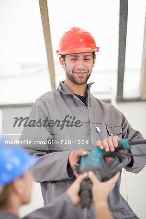 Male and female laborer handing electric drill on construction site