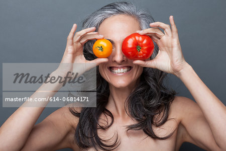 Mature woman covering eyes with red and yellow tomato