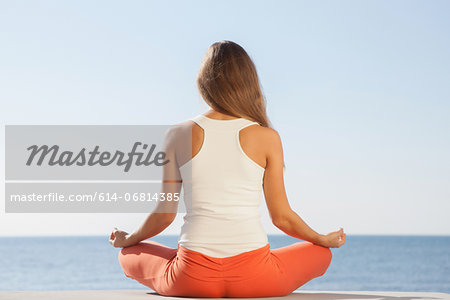 Young woman meditating by sea rear view