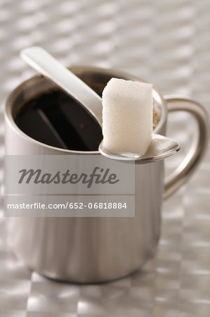 Cup of black coffee with a teaspoon and a sugar lump