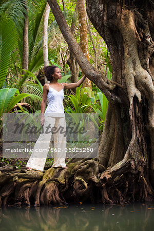 Dominica, Portsmouth. A young woman stands on a tree on the Indian River, one of Dominica's most popular tourist attractions. (MR).