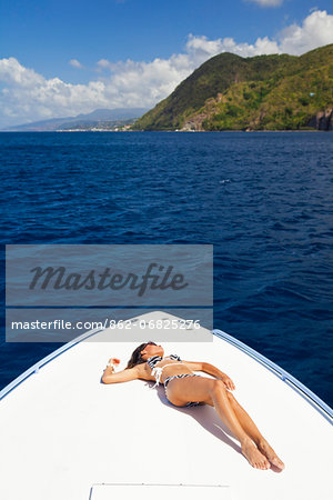 Dominica, Soufriere. A young woman sunbathes on the foredeck of a Powerboat near Soufriere. (MR).