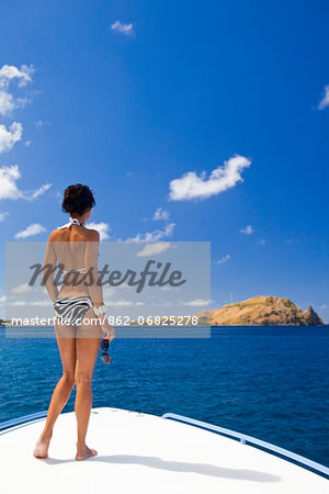 Dominica, Soufriere. A young woman stands on the foredeck of a Powerboat near Soufriere, looking at Scott's Head - a distinctive landmark of Dominica. (MR).