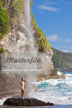 Dominica, Riviere Cyrique. A young woman stands under the waterfall at Wavine Cyrique. (MR). Dominica, Riviere Cyrique. A young woman stands under the waterfall at Wavine Cyrique. (MR).