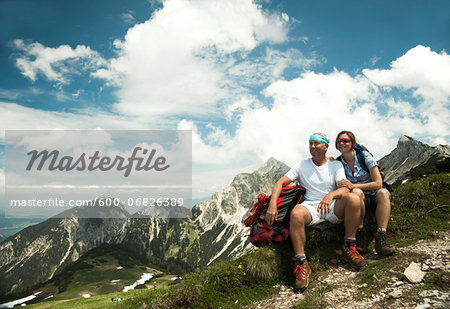 Mature couple sitting on grass, hiking in mountains, Tannheim Valley, Austria