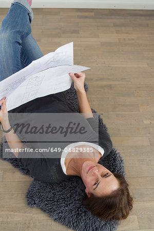 Woman lying on floor holding blueprints