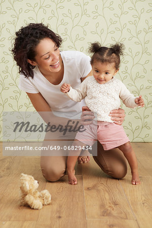 Mother holding baby girl taking first steps, smiling