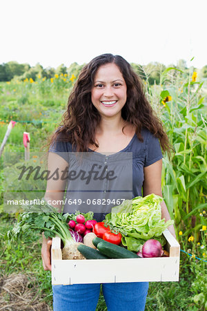 Portrait of young woman holding box of fresh vegetables in allotment