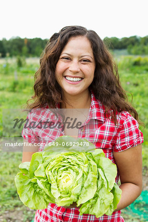 Portrait of young woman holding cabbage in allotment