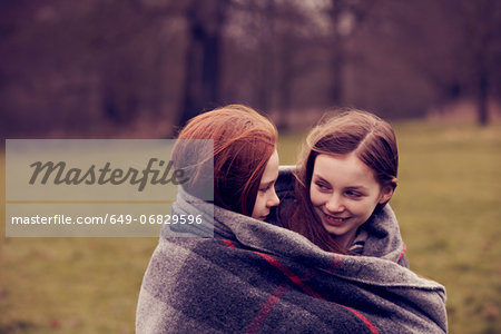 Girls wrapped in a blanket outdoors, smiling Girls wrapped in a blanket outdoors, smiling