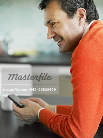 Mature man using cellphone in kitchen
