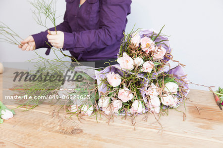 Close up of young florist arranging plants and roses into bouquet