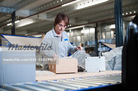 Female warehouse worker packing box for conveyor belt