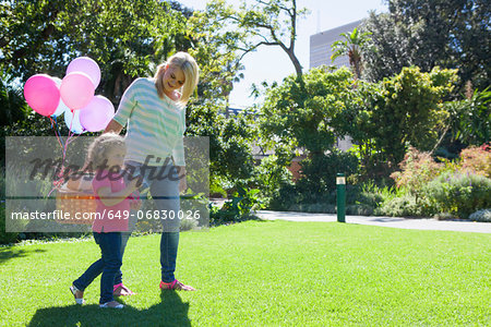 Mother and daughter walking in garden with basket of balloons