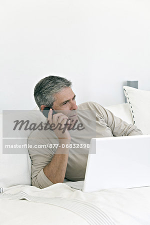 Senior man phoning, in front of a laptop