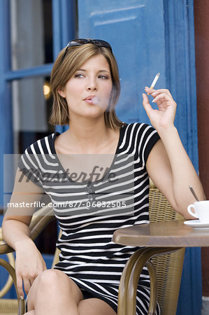 Young woman sitting at coffee shop terrace, smoking