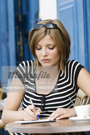 Young woman sitting at coffee shop terrace, writting