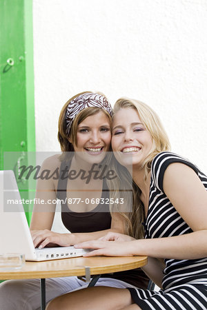 Two young women posing for the camera, laptop