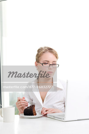 Woman eating cake while using laptop computer