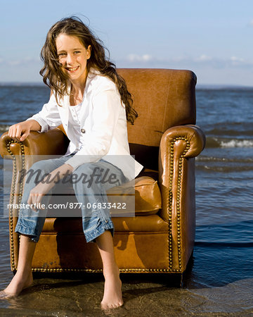 Little girl sat in brown leather armchair, at the edge of a lake