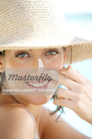 Portrait woman smiling, straw hat, putting sun lotion on cheeks and nose