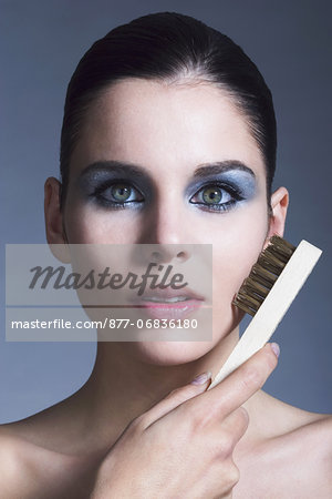 Portrait of a young woman using steel brush on her cheek