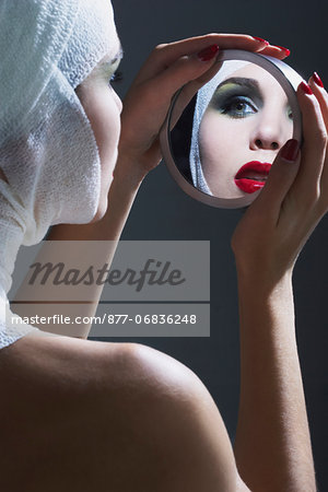 Young woman looking in a mirror, bandages on head