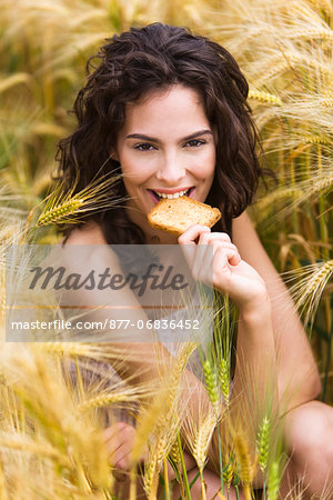 Young woman in wheat field, eating a rusk