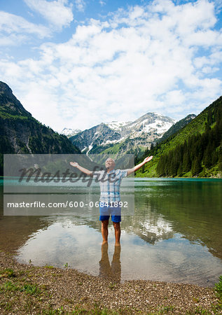 Mature man with arms stretched outward, standing in Lake Vilsalpsee, Tannheim Valley, Austria