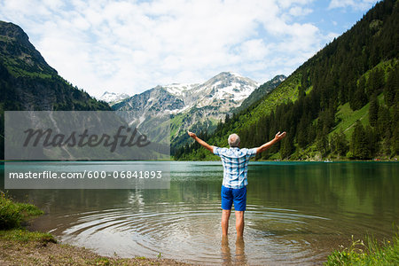 Backview of mature man with arms stretched outward, standing in Lake Vilsalpsee, Tannheim Valley, Austria