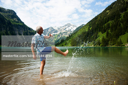 Mature man standing in lake, kicking water, Lake Vilsalpsee, Tannheim Valley, Austria