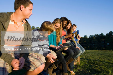 Group of pre-teens sitting on fence, looking at tablet computer and cellphones, outdoors, Florida, USA