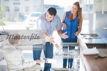 Couple and salesman looking at dishwasher in kitchen showroom