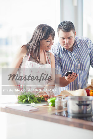 Couple looking at smartphone whilst preparing food