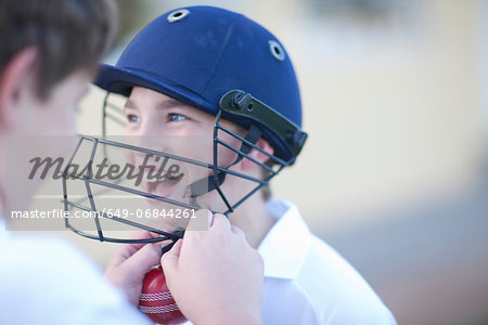 Boy putting cricket helmet on another boy